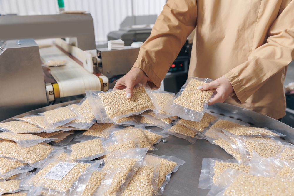 A woman in a production line handling vacuum packaged bags of nuts.