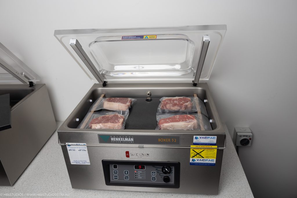 A Henkelman vacuum packaging machine with meat prepped inside to vacuum packaged. 