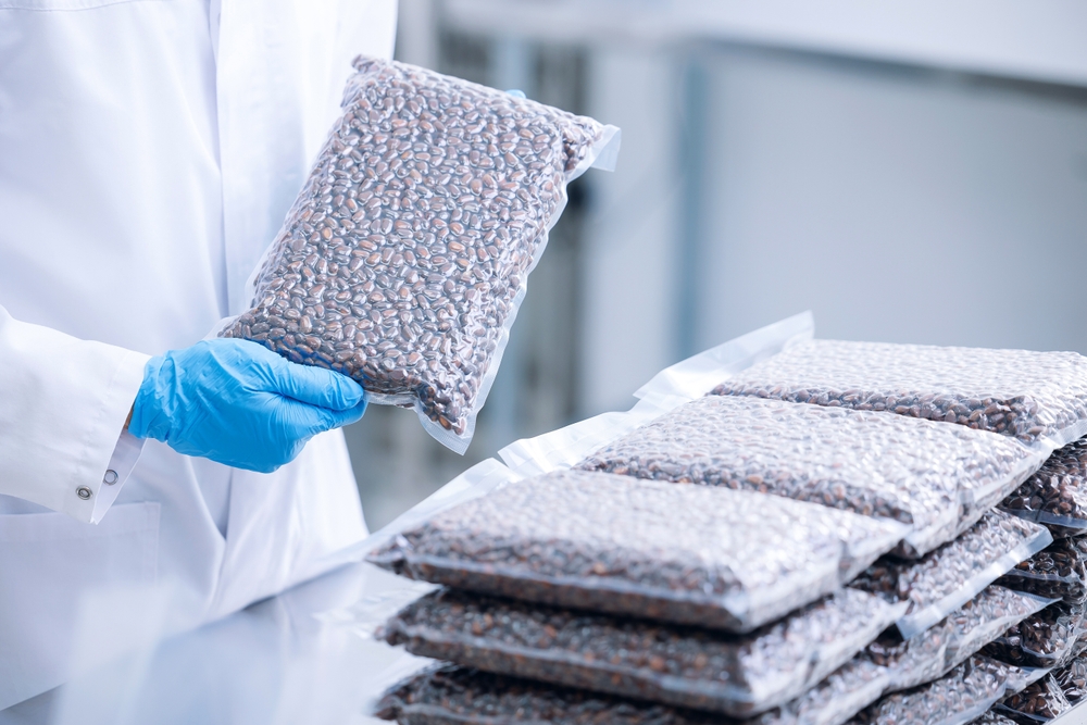 A person holding a bag of vacuum sealed nuts with a pile of more bags nearby. 