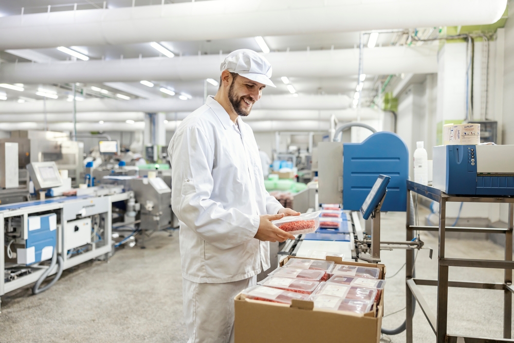A factory worker inspecting meat that has been vacuum sealed.