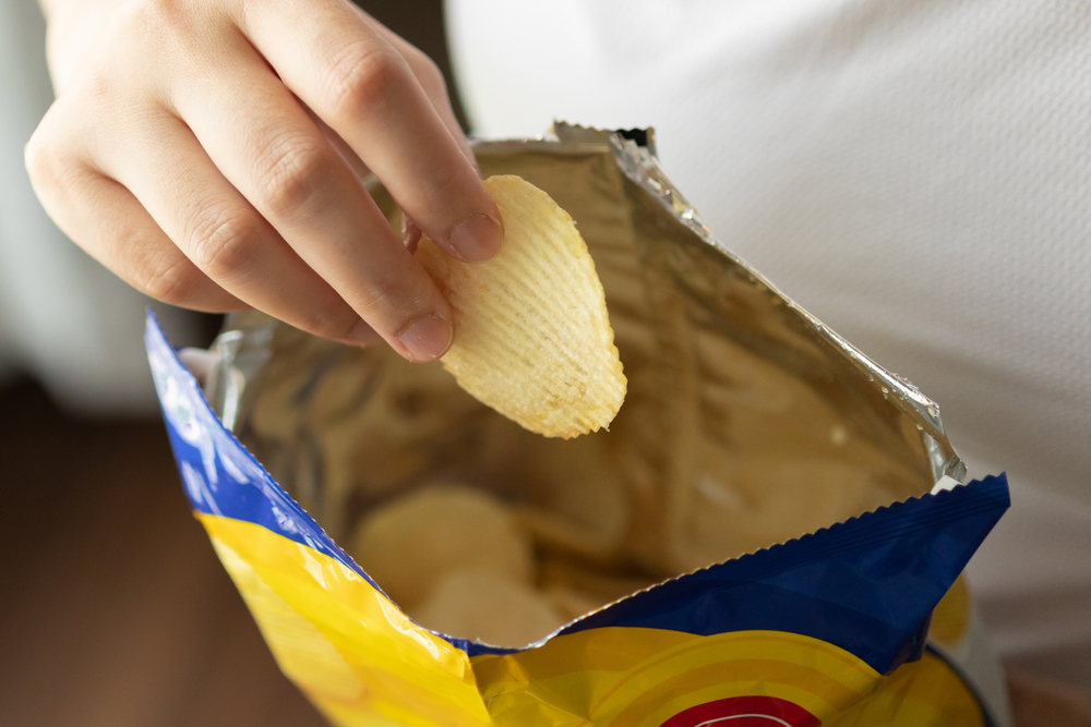 A had pulling a fresh chip out of a bag that has been packaged using the gas flush feature on a vacuum packaging machine.