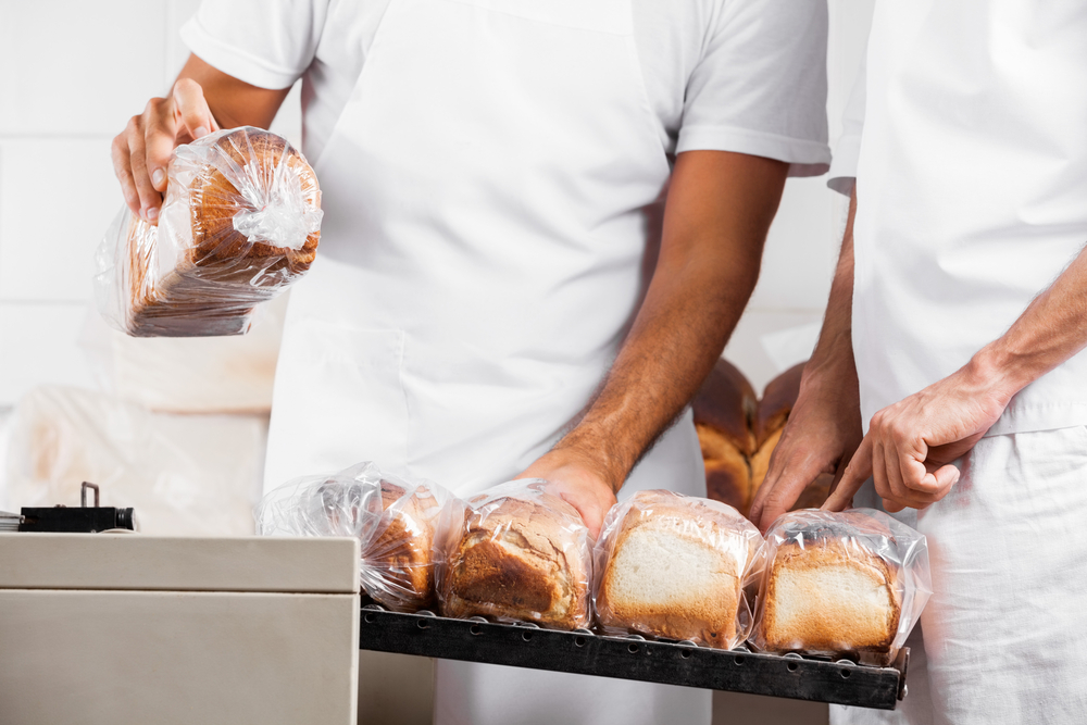 Bakers packaging loaves of bread using a vacuum sealing machine with a gas flush feature.